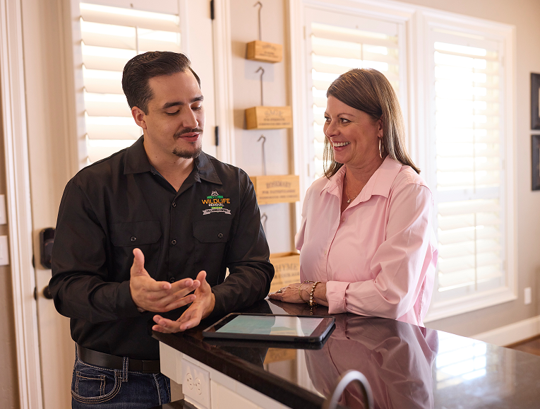 friendly_consultation Wildlife removal specialist explaining service details to a smiling homeowner in a well-lit kitchen, showcasing trust and clear communication.