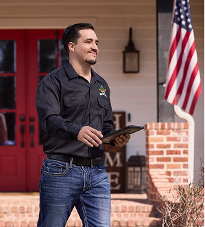 service_success Wildlife technician walking confidently away from a home with a tablet in hand, smiling after completing a service visit, with an American flag and red door in the background.